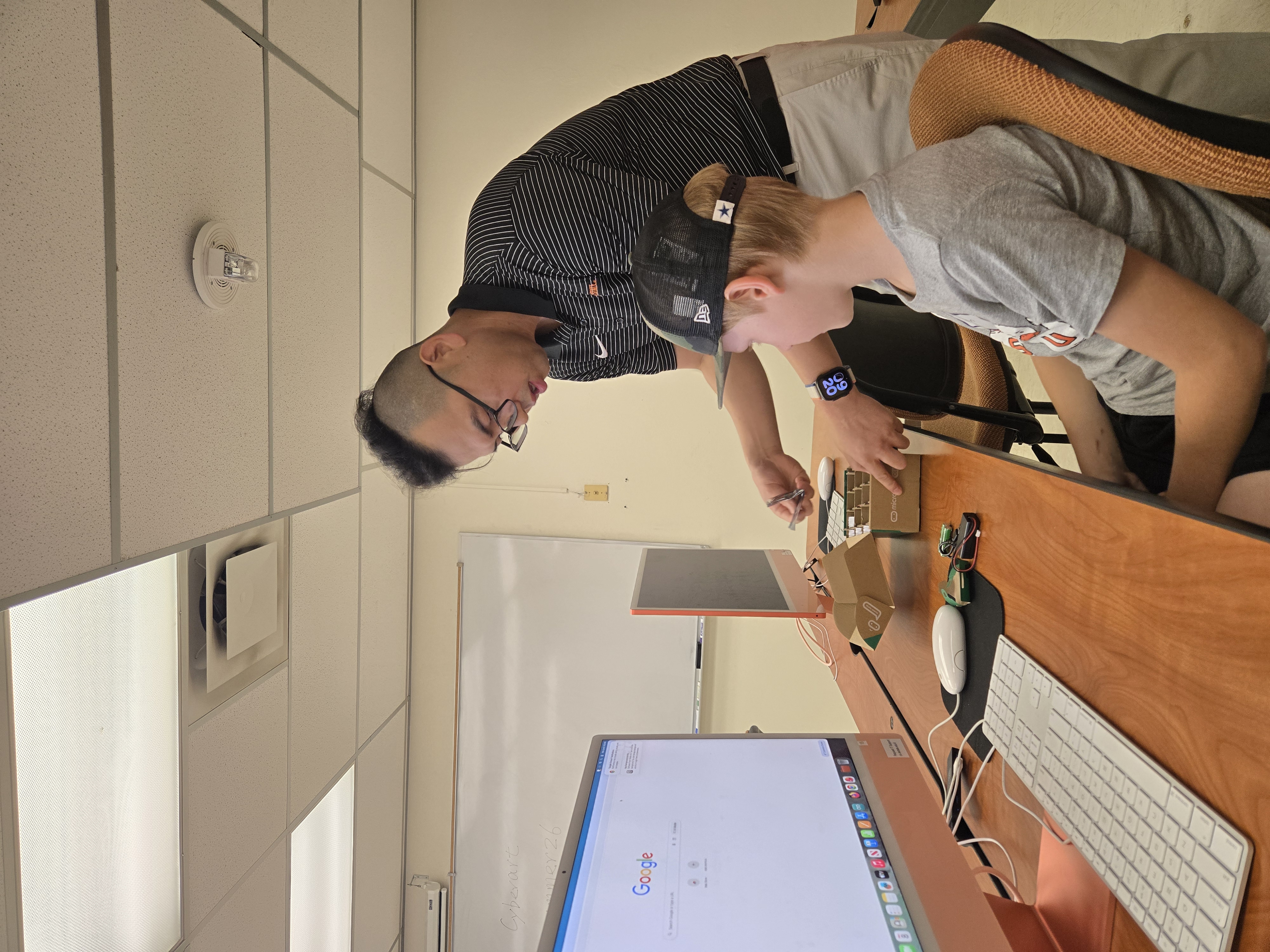 A professor assists a student seated at a computer during a classroom