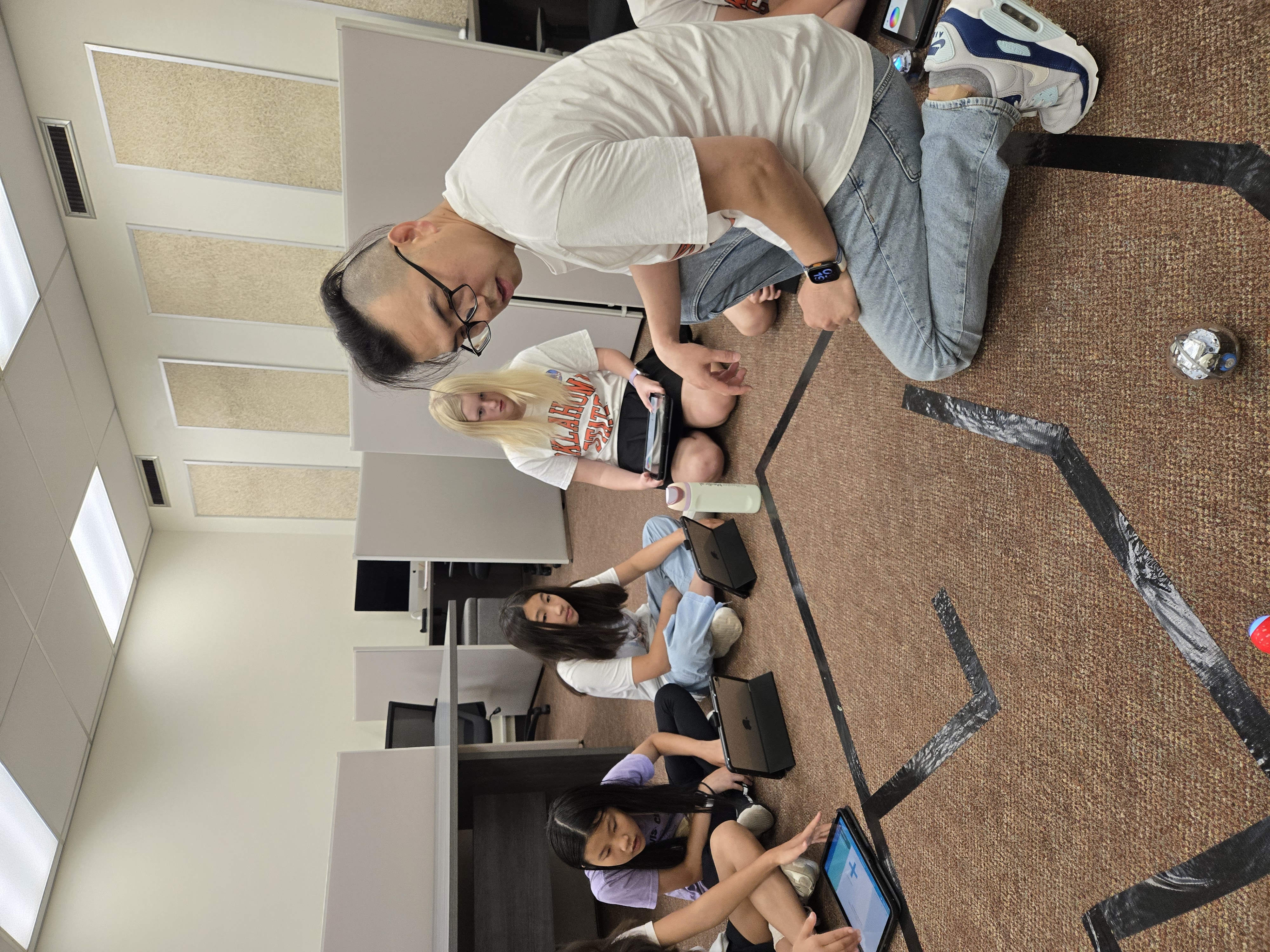 instructor kneels on the floor demonstrating a small programmable robot