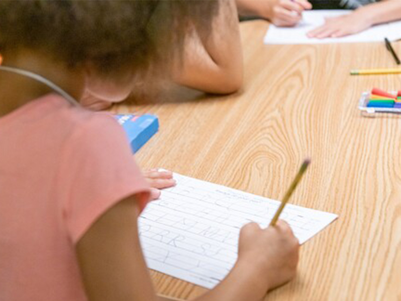 girl writing on a piece of paper at a table