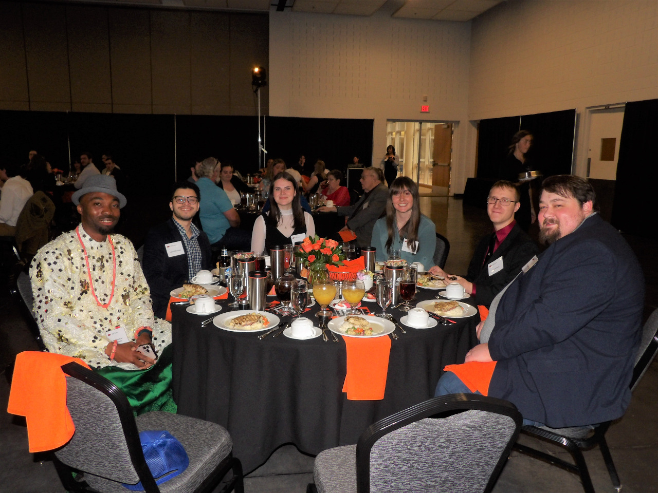 Four male and two female students sitting down and enjoying each others company during banquet.