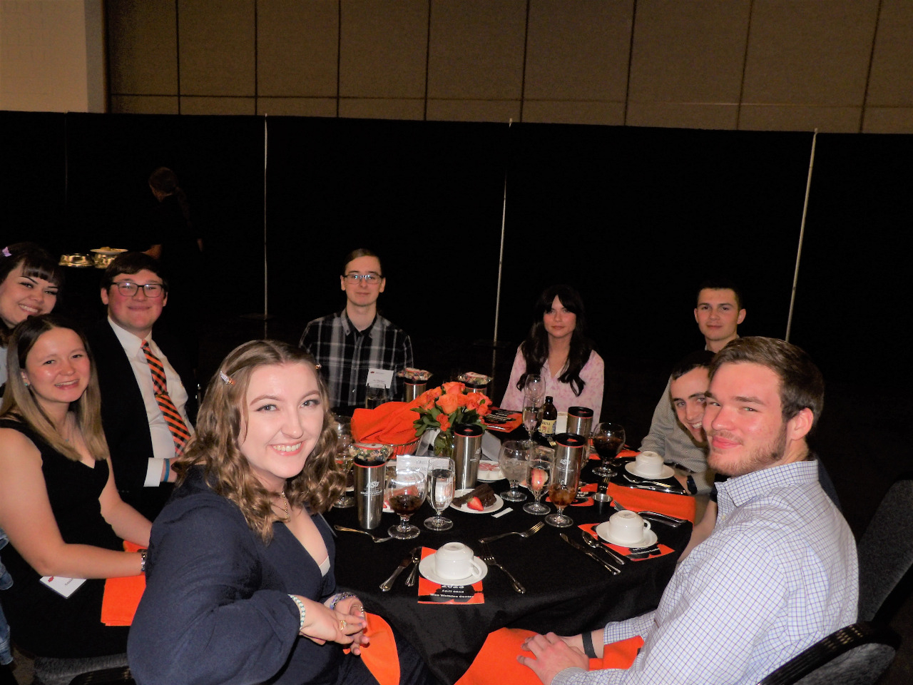 Five male and four female students hanging out at the dinner table before banquet begins.