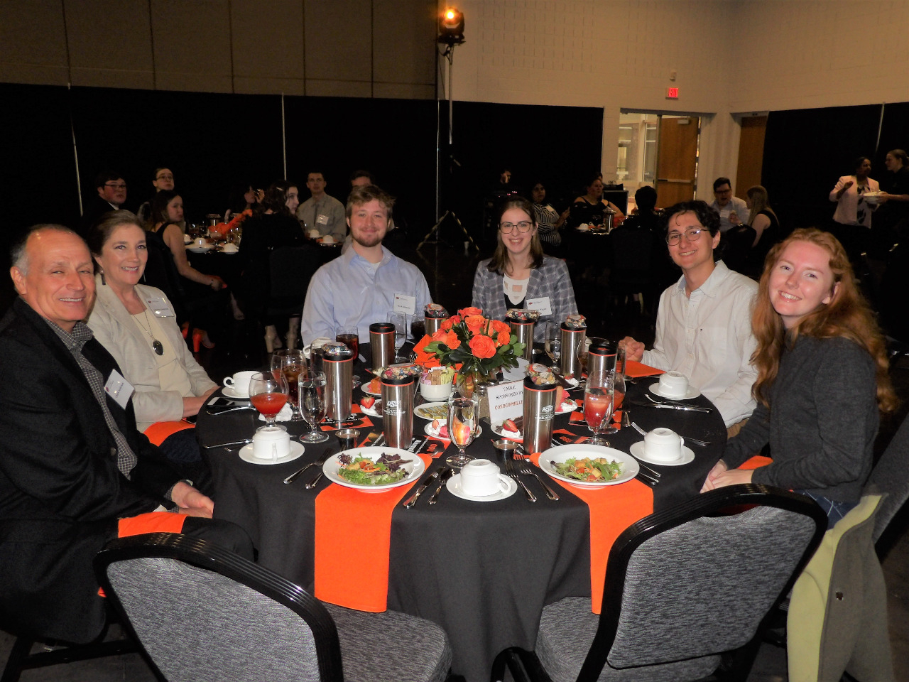 Two female and two male students sitting with one male and one female alumni at the dinner table.