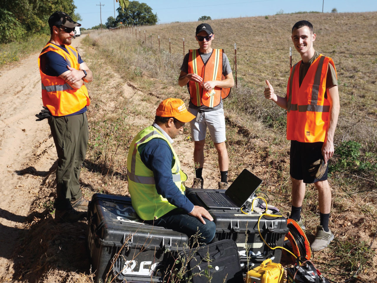 Three male students, watching Dr. Ahmed Isamil using a computer in the field.
