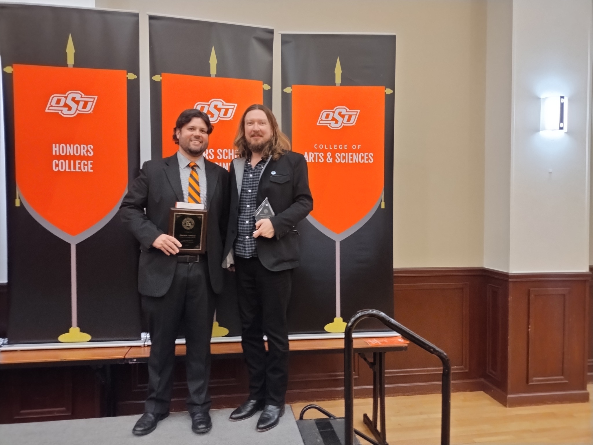 Two men standing with awards against an orange and black background