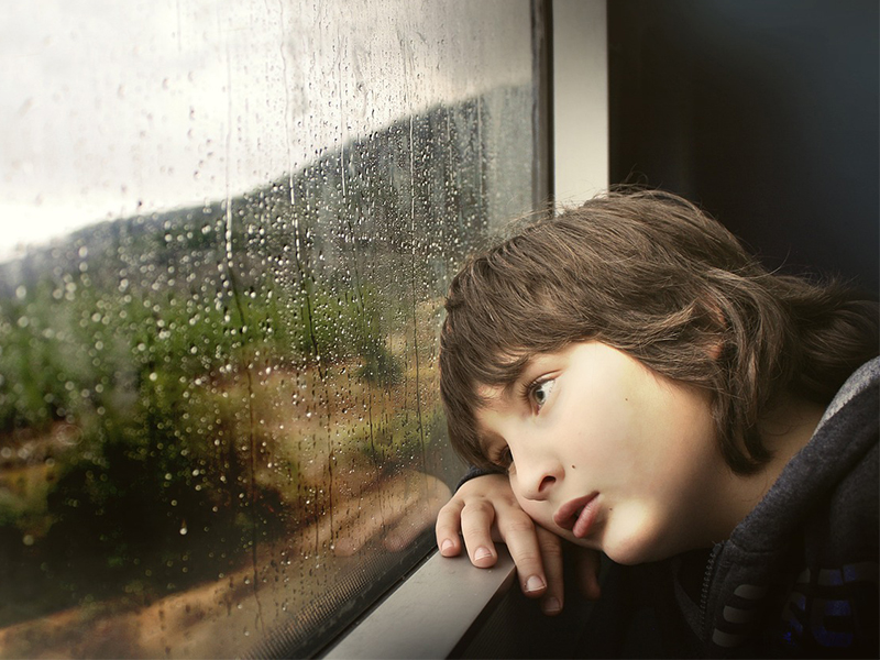 boy staring out window with rain dripping down it.