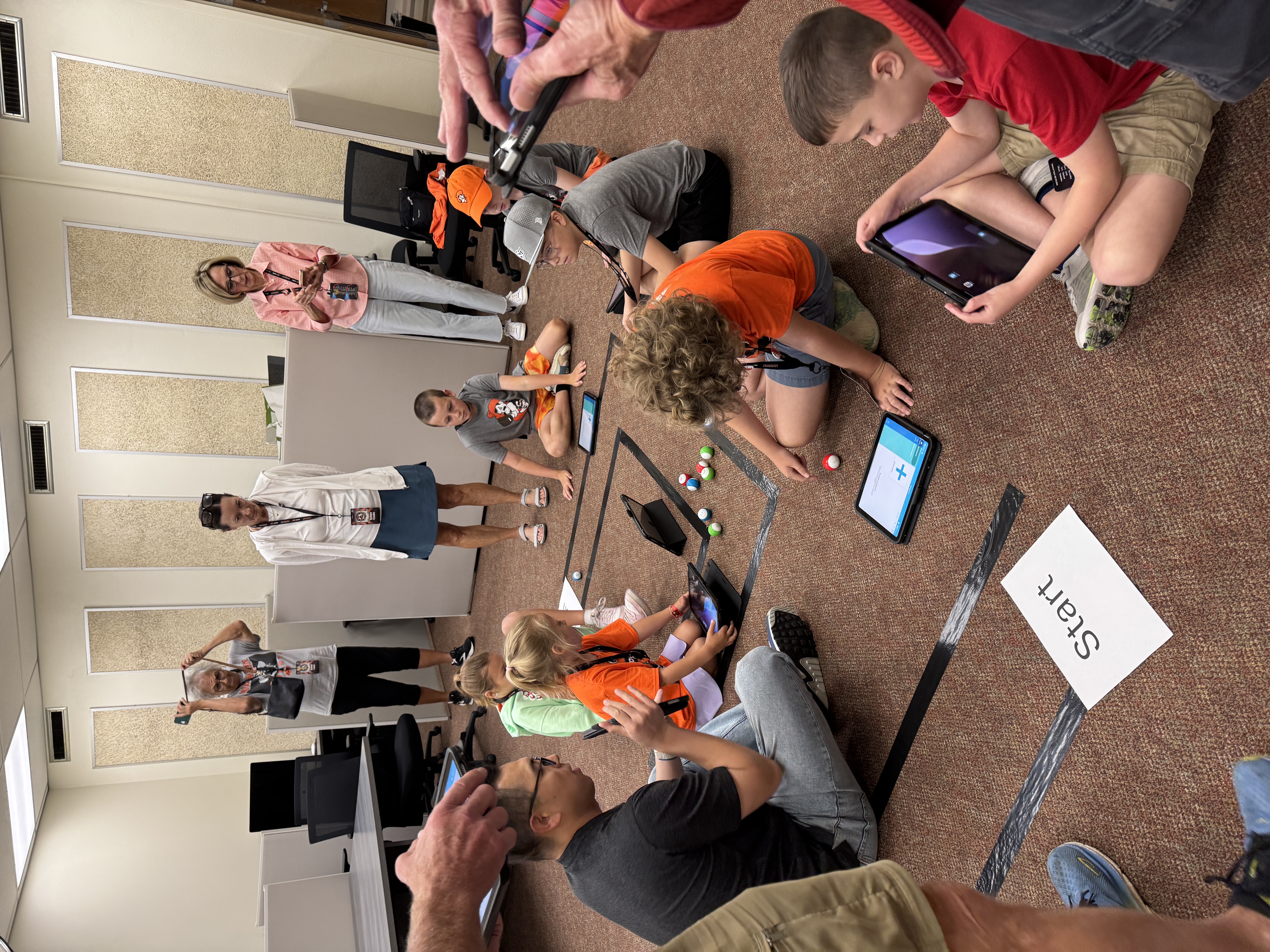 Students sitting on the floor during a class activity, working with small robots.
