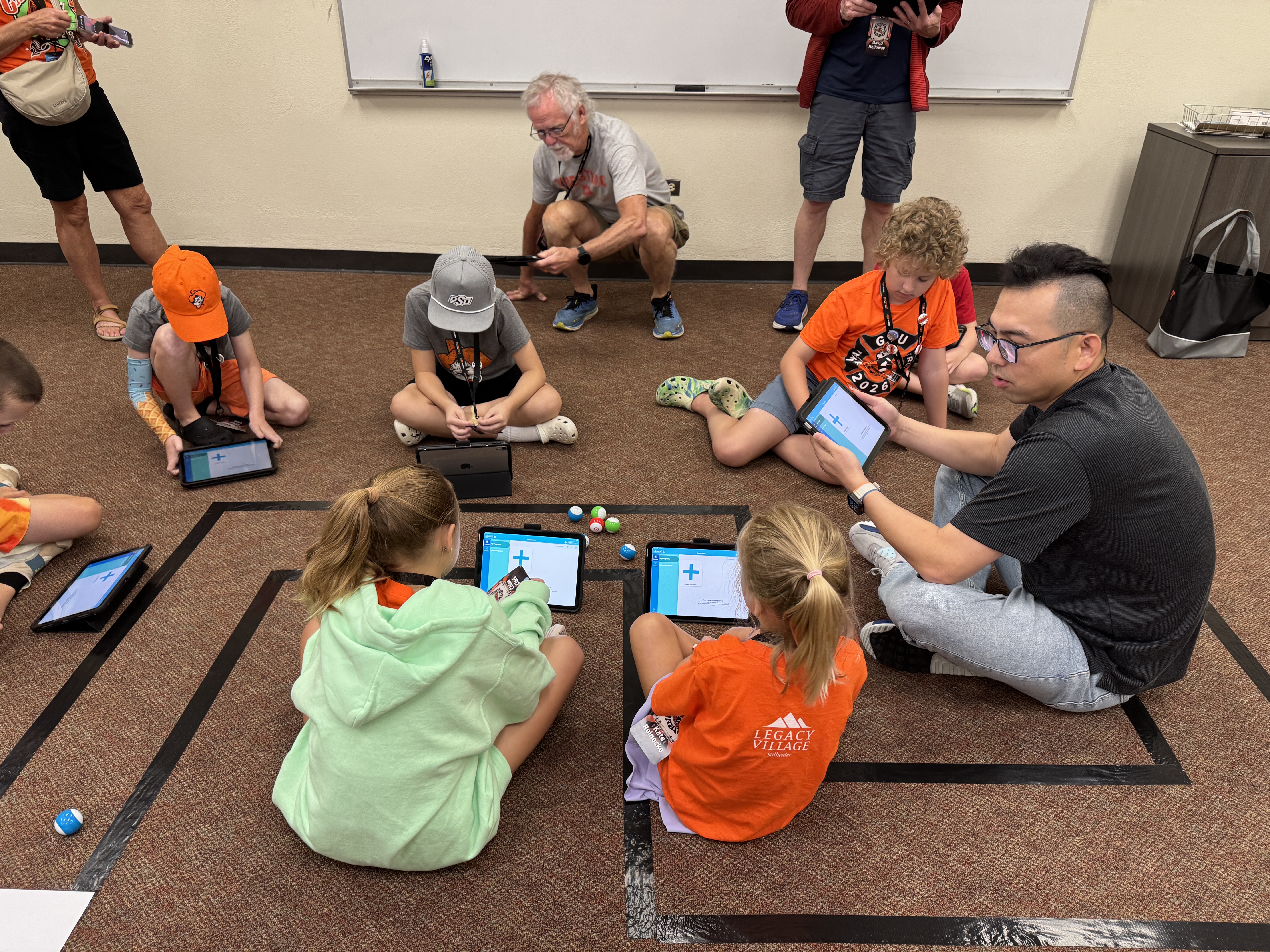 Students sitting on the floor during a class activity, working with small robots.