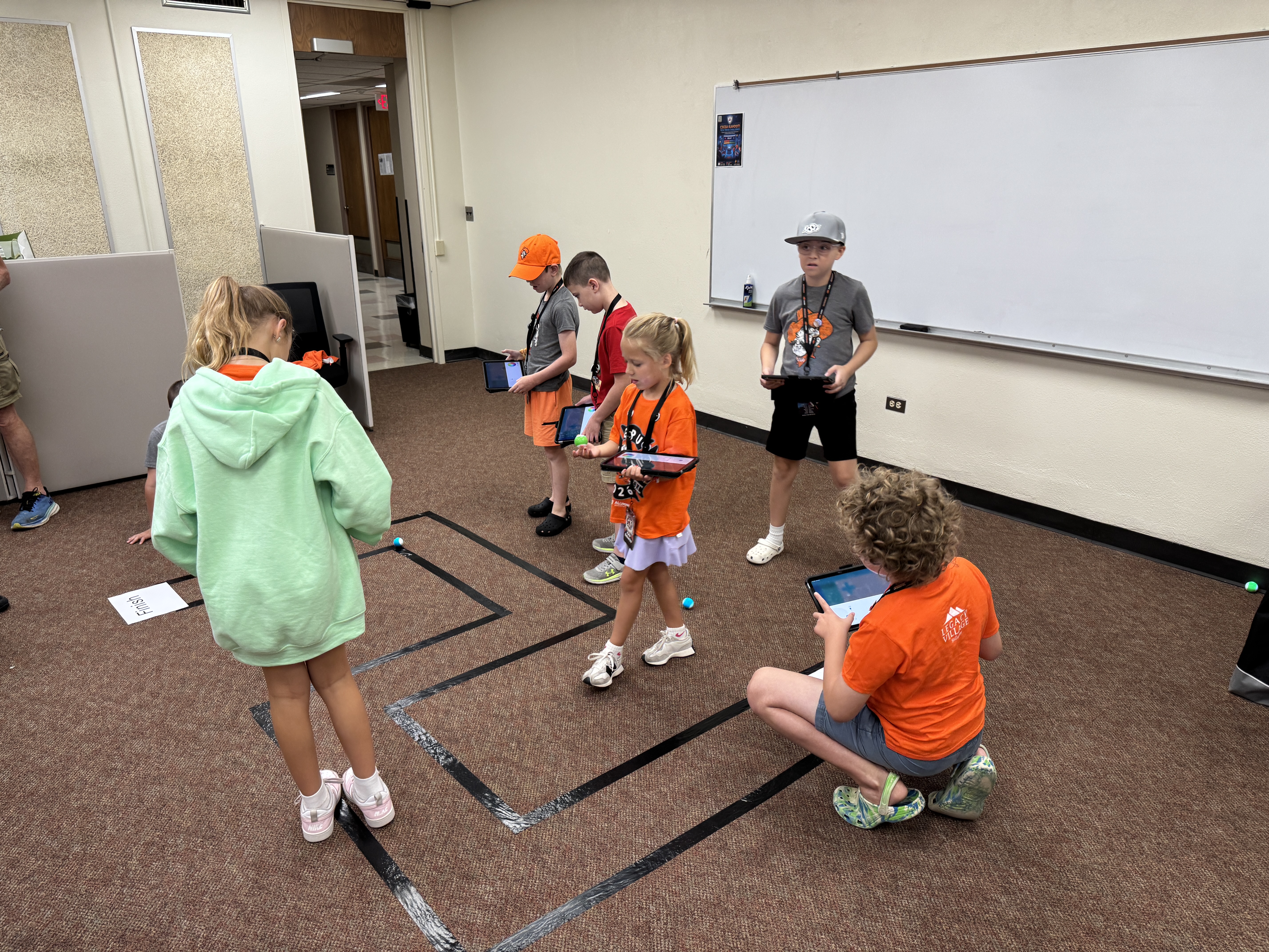 Students sitting on the floor during a class activity, working with small robots.