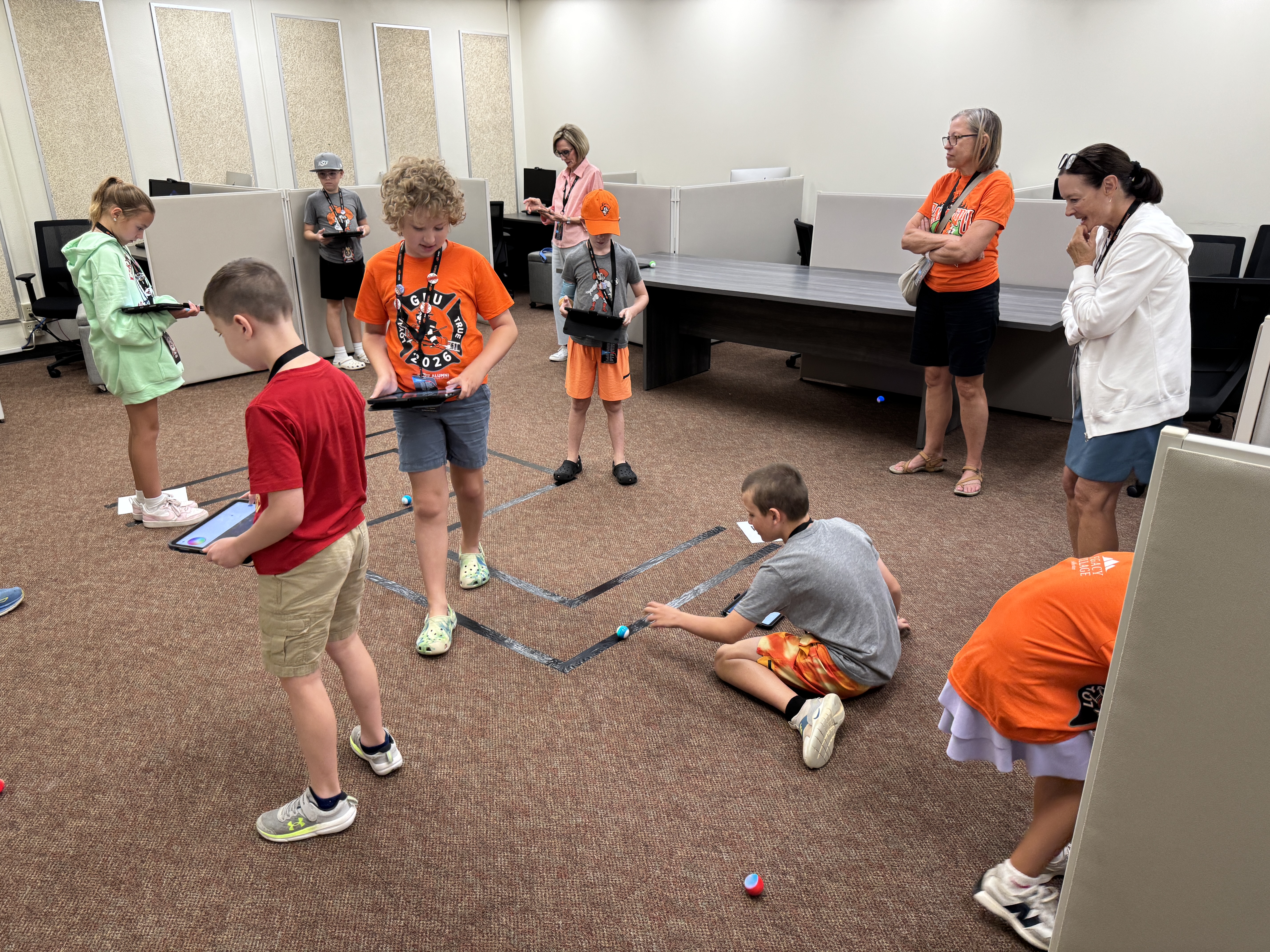 Students sitting on the floor during a class activity, working with small robots.
