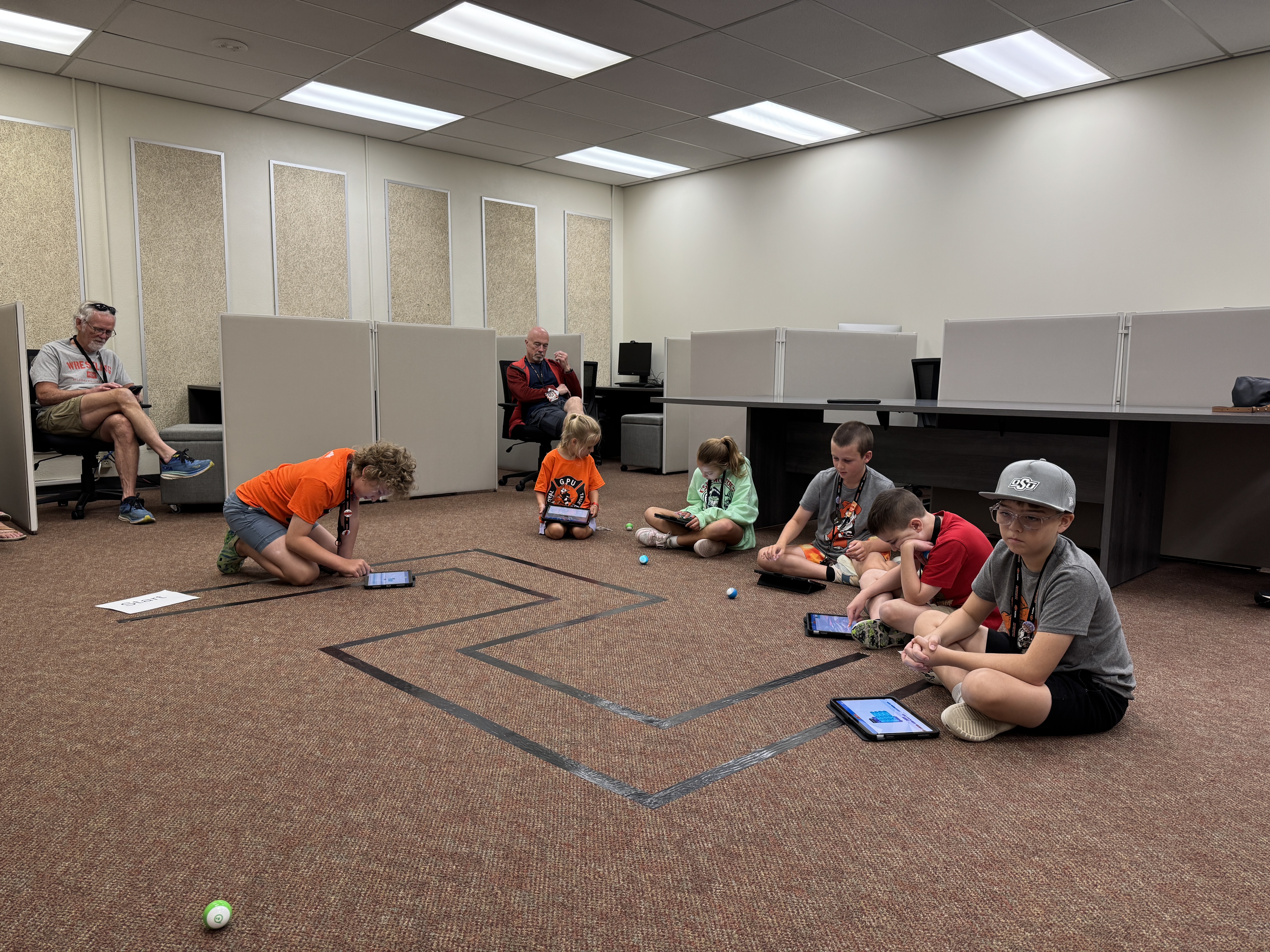 Students sitting on the floor during a class activity, working with small robots.