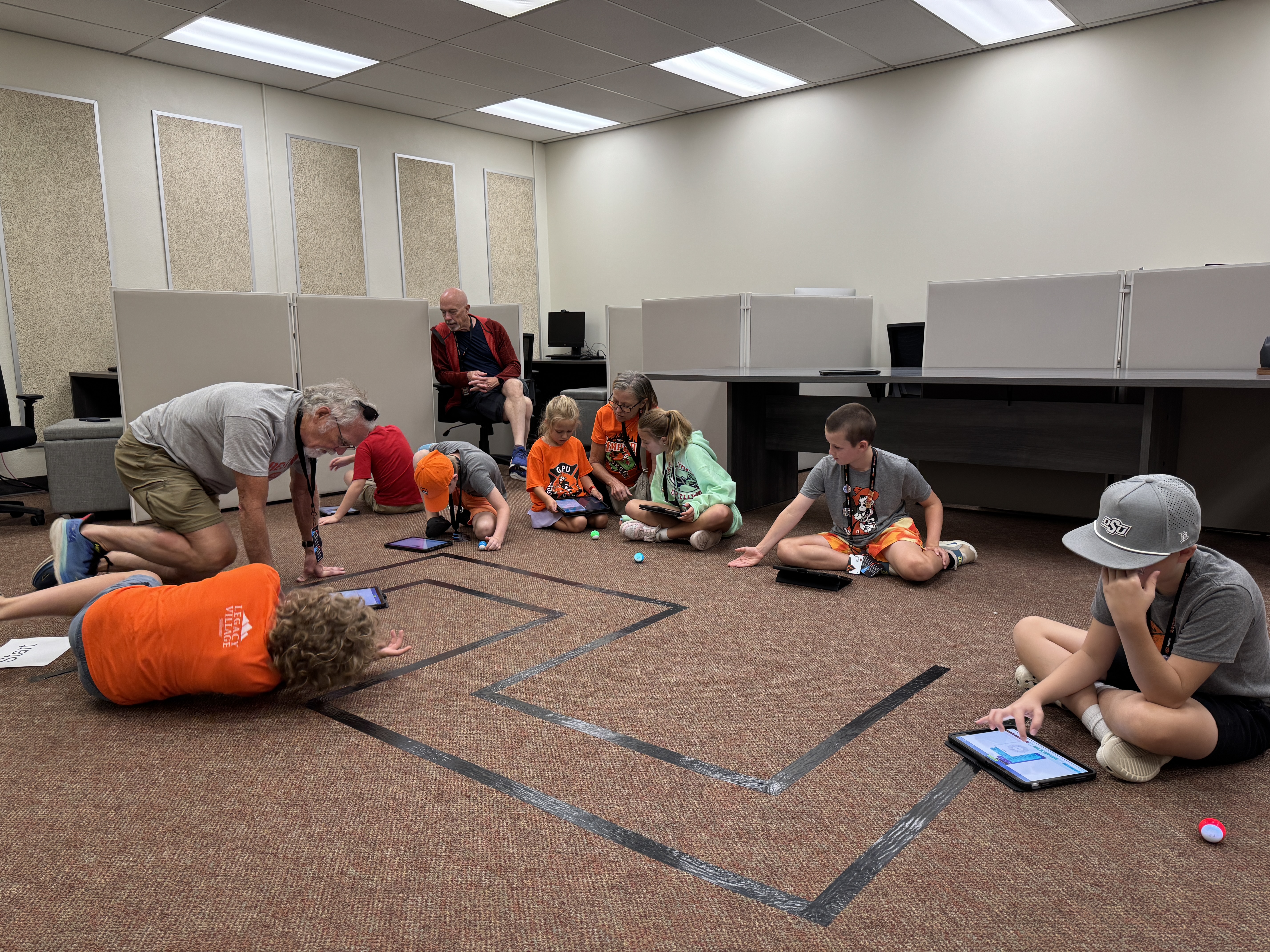 Students sitting on the floor during a class activity, working with small robots.