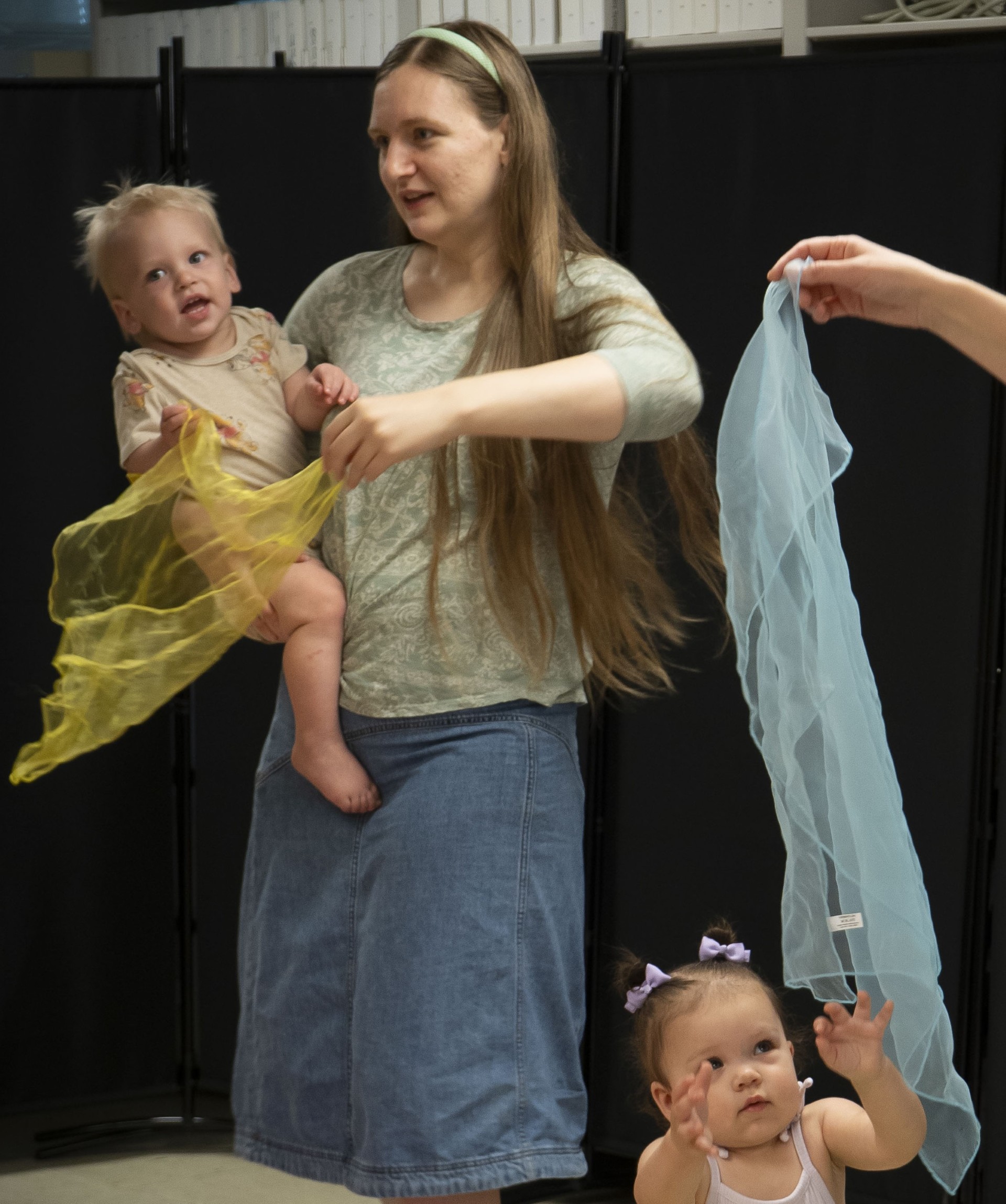 A woman holding a toddler while moving a colorful Silk scarves.