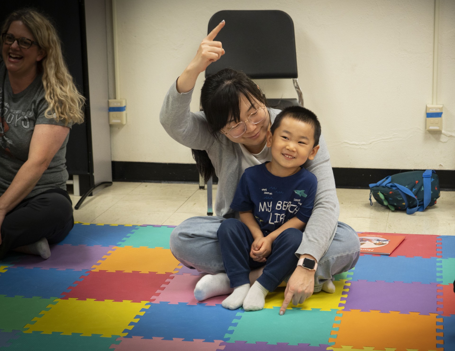A boy sitting on a woman’s lap, listening to music together.