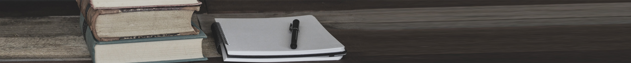 Close-up of old books, a notebook, and a pen on a table